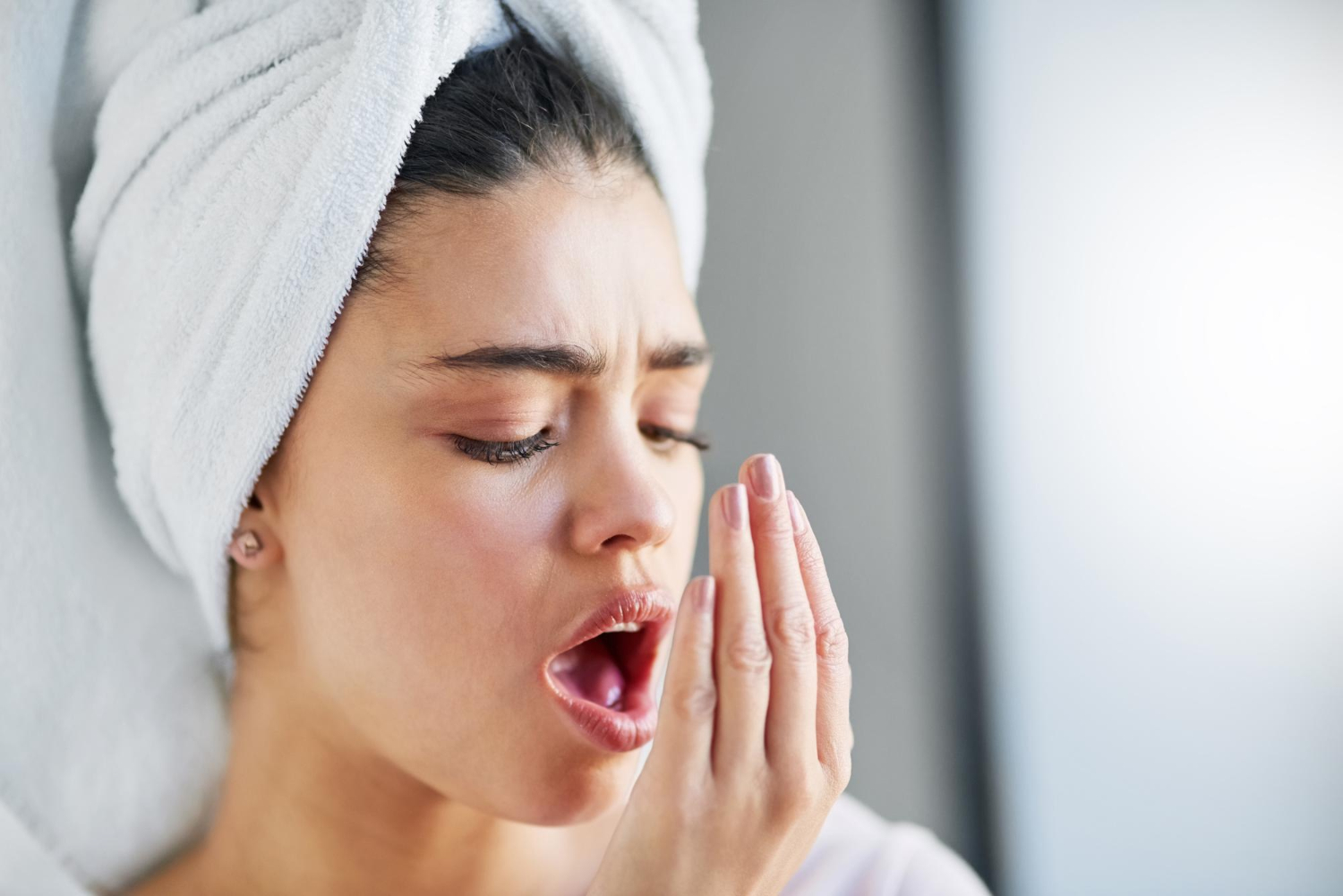 donna con asciugamano in testa mette la mano davanti la bocca e alita